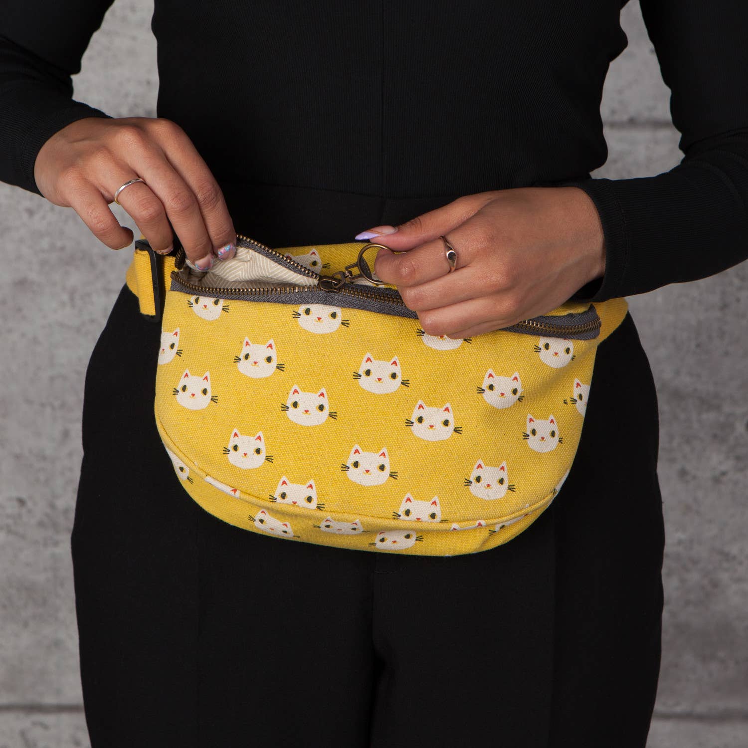 A close-up of the Meow & Go Fanny Pack with yellow fabric and cute cat face designs, being opened to reveal its roomy interior.