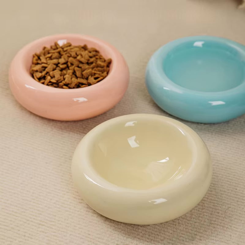 A set of five sleek, round ceramic cat bowls in assorted colors with dry food inside.