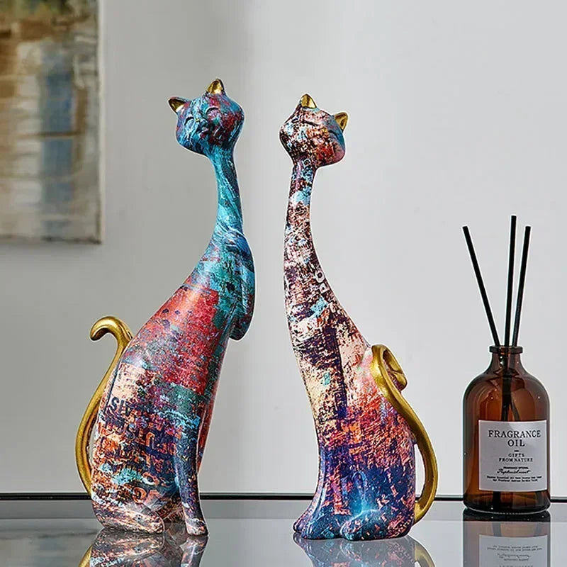 Pair of artistic cat figurines with sleek designs, vibrant patterns, and gold accents, displayed on a table for home décor.