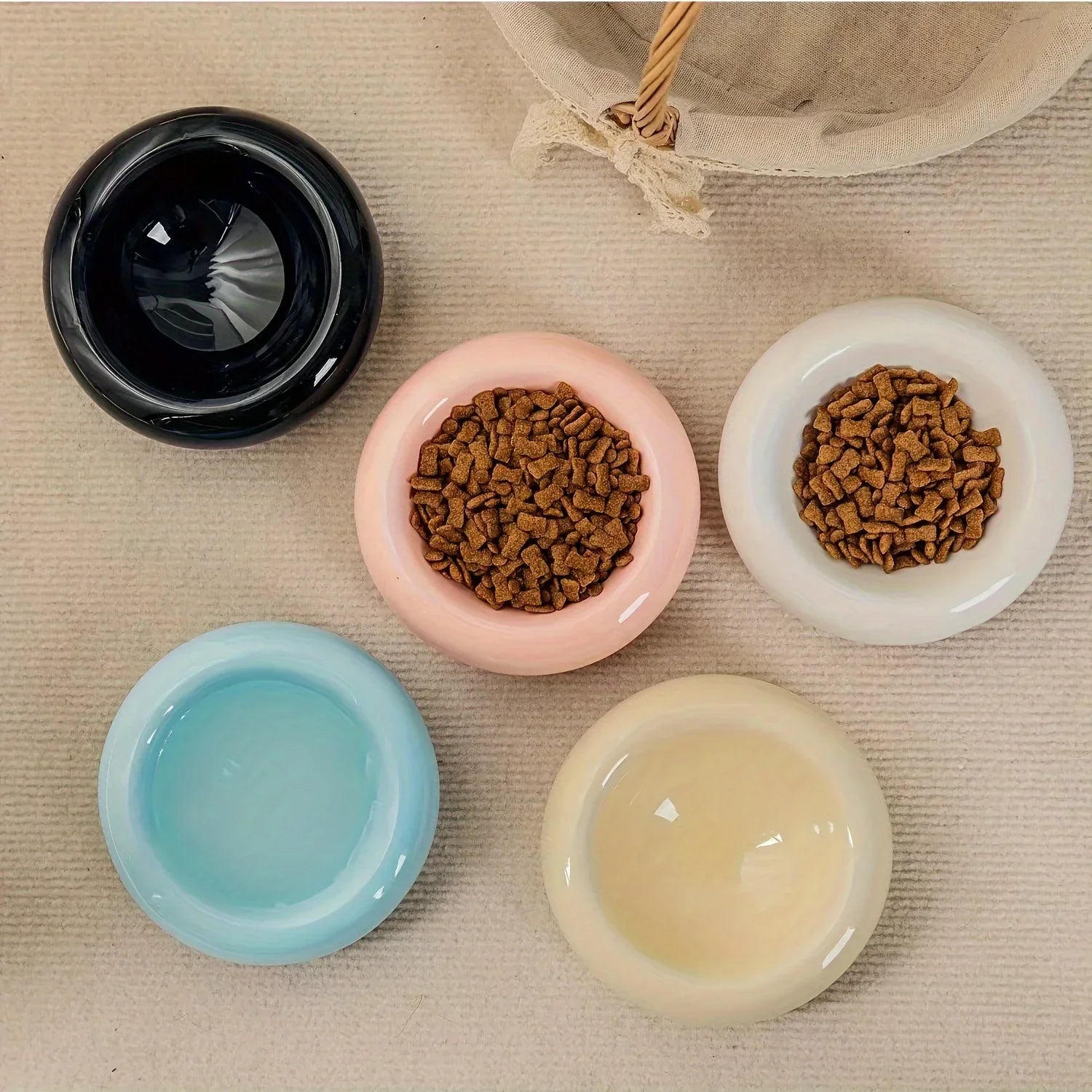 A set of five sleek, round ceramic cat bowls in assorted colors with dry food inside.