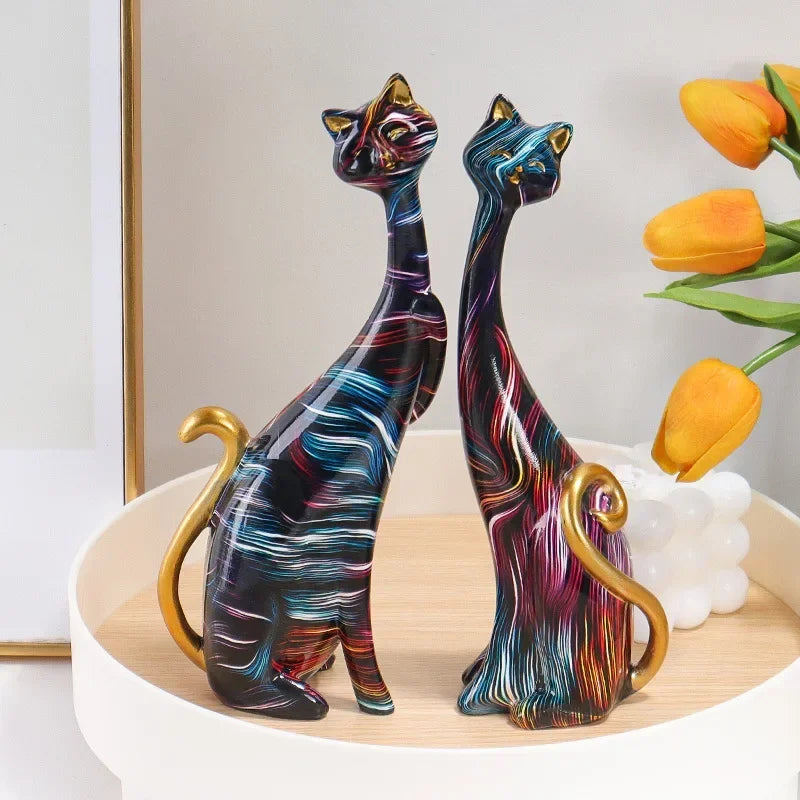 Pair of artistic cat figurines with sleek designs, vibrant patterns, and gold accents, displayed on a table for home décor.