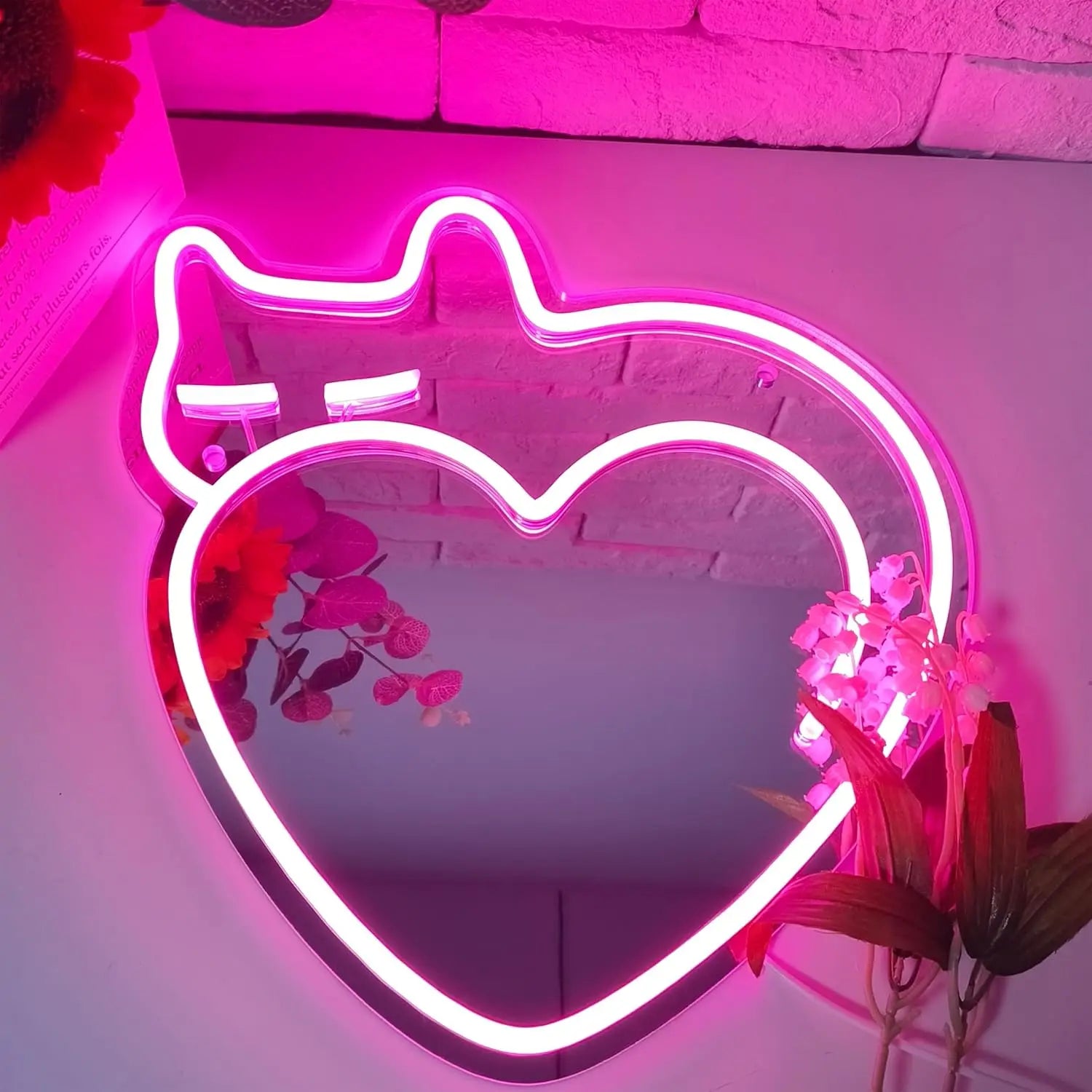 Pink neon Cat Heart Mirror with glowing cat ears on a table, reflecting vibrant sunflowers and soft decor.