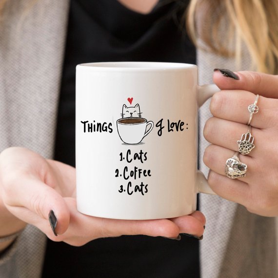Woman holding funny coffee mug about coffee and cats 